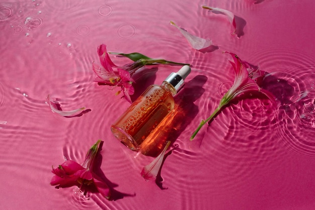 Witaminowe serum witaminowe w szklanej butelce w wodzie otoczonej kwiatami na różowo
