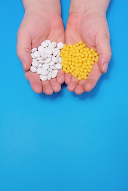 Witaminy w rękach dorosłego białe tabletki i żółte kapsułki na niebieskim tle, centralne v
