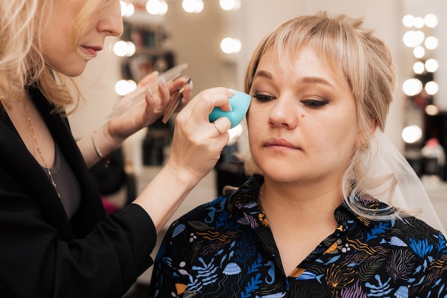 Wizażystka cieniuje podkład na skórze modelki za pomocą beauty blendera.