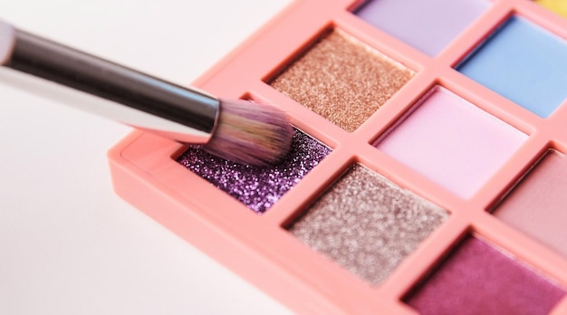 Wizażystka wybiera za pomocą pędzelka fioletowy połyskujący pigment z palety jasnych kolorowych cieni do powiek