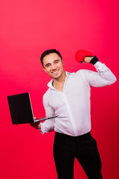 Wizerunek młodego wesołego biznesmena w zegarku trzymającego i używającego laptopa izolowanego na czerwonym tle