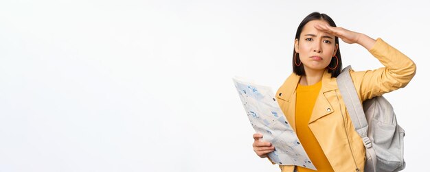Wizerunek młodej azjatyckiej dziewczyny turysty z mapą i plecakiem pozuje na białym tle studia