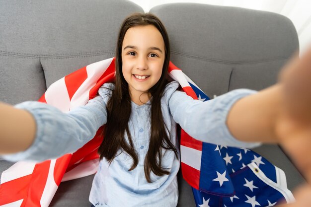 Wizerunek pięknej wesołej małej dziewczynki z dużą amerykańską flagą.