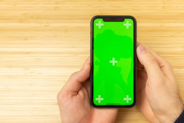 Wizerunek ręki trzyma czarnego telefon komórkowego z zieleń ekranem na biurowym stole z kopii przestrzenią.