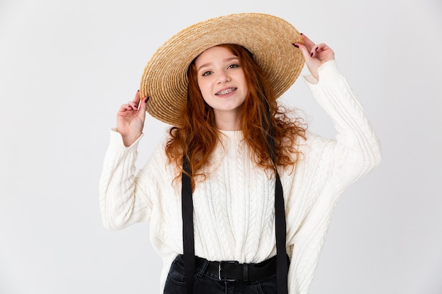 Wizerunek rudowłosy piękny młody ładny dziewczyna pozowanie na białym tle na tle białej ściany na sobie kapelusz.