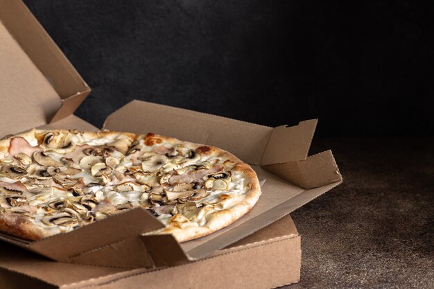 Właśnie dostarczono pizzę w kartonie, pokrojoną pizzę z szynką i pieczarkami, selektywne skupienie