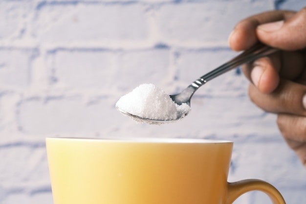 Wlewanie białego cukru do filiżanki herbaty
