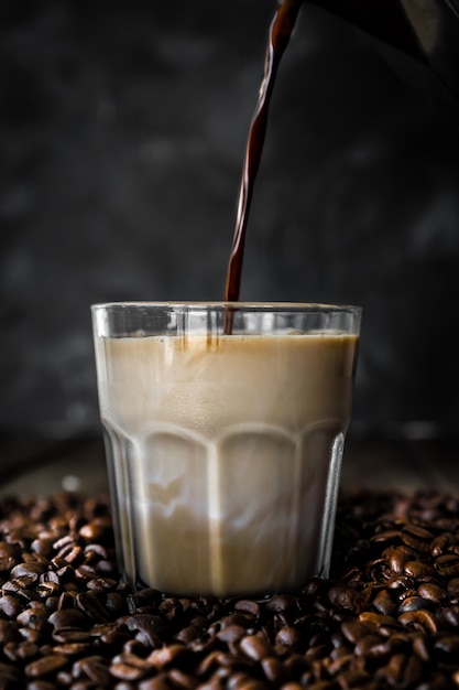 Zdjęcie wlewanie kawy do szklanki mleka z tłem ziaren kawy