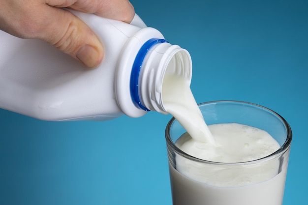 Wlewanie mleka z białej plastikowej butelki do szklanki na niebieskim tle