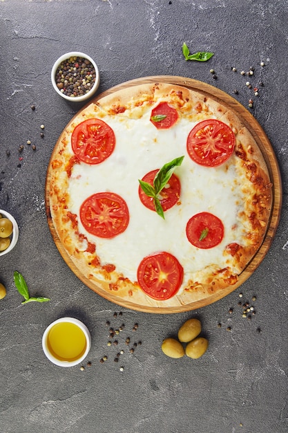 Włoska pizza i składniki dla gotować na czarnym betonowym tle. Pomidory, oliwki, bazylia i przyprawy. Skopiuj miejsce na tekst.