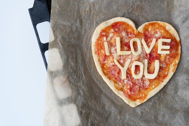 Włoska pizza w kształcie serca z salami, sosem pomidorowym, parmezanem, sosem do pizzy, mozzarellą i oliwą z oliwek na papierze pergaminowym z serem. Kocham cię Koncepcja miłości na Walentynki 14 lutego