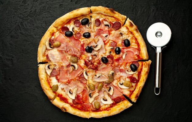 Włoska pizza z bekonem, pieczarkami, oliwkami, pomidorami na czarnym betonowym tle