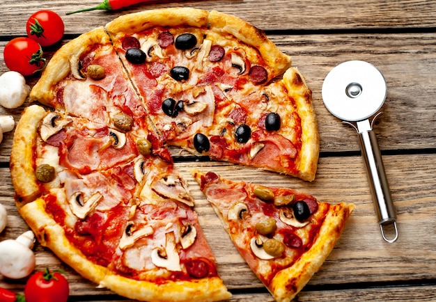 włoska pizza z boczkiem, pieczarkami, oliwkami, pomidorami na tle drewna