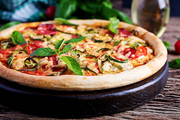 Włoska pizza z kurczakiem, salami, cukinią, pomidorami i ziołami na vintage drewnianym stole. Kuchnia włoska