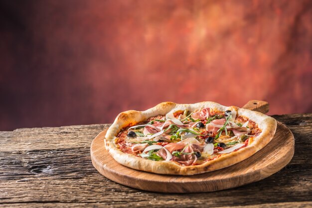 Włoska pizza z prosciutto pomidorkami oliwkami oliwą parmezanem i rukolą