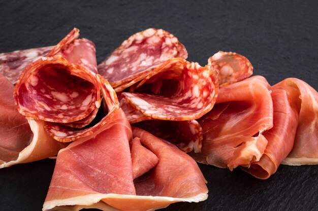 Włoska prosciutto crudo lub hiszpańska szynka i kiełbaski. Surowa szynka na kamiennej desce do krojenia