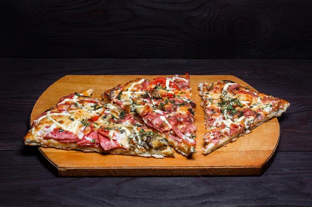 Włoska rustykalna pizza trzy kawałki na drewnianej tacy ciemny drewniany stół