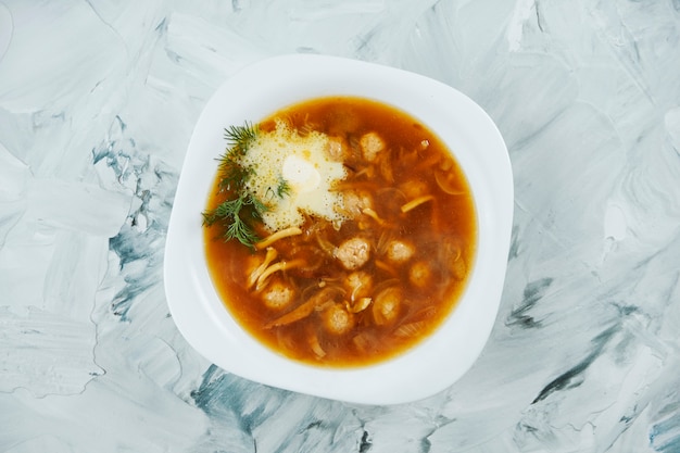 Włoska zupa z makaronem i cielęcym rossini z masłem w białej misce na szarym stole.