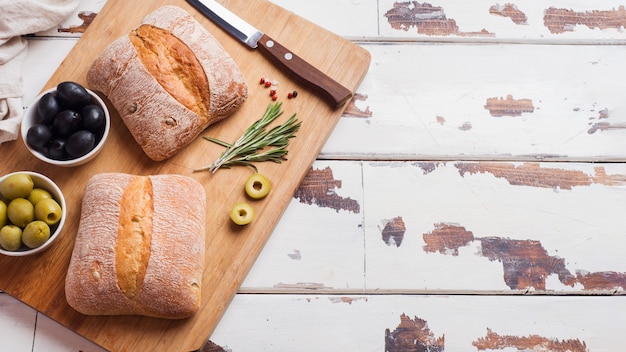 Włoski chleb ciabatta z oliwkami i rozmarynem na drewnianej desce. Skopiuj miejsce