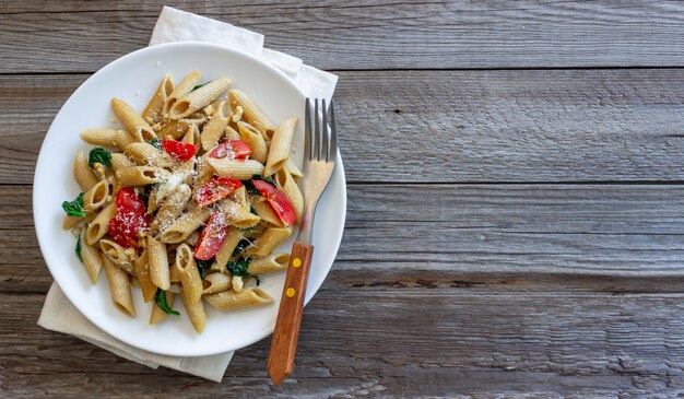 Włoski makaron penne z pomidorami, szpinakiem, parmezanem, czosnkiem i orzechami. Zdrowe odżywianie. Jedzenie wegetariańskie.