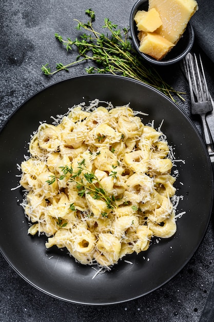 Włoski makaron Tortellini z parmezanem. Czarne tło. Widok z góry