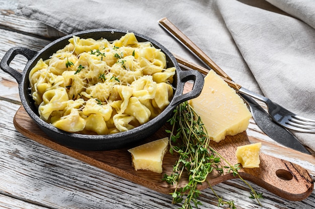 Włoski makaron Tortellini z parmezanem na patelni. Białe drewniane tła. Widok z góry