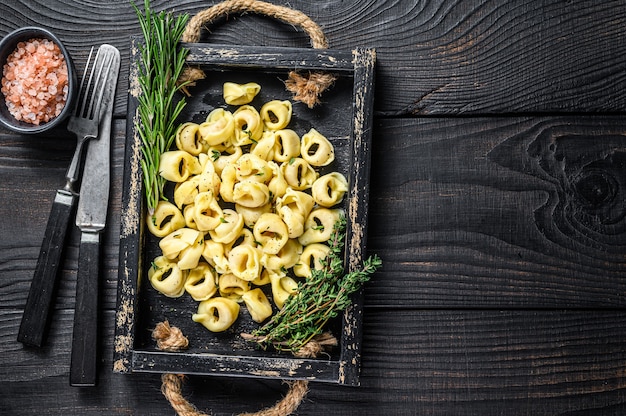 Włoski tradycyjny makaron tortellini ze szpinakiem w drewnianej tacy. Czarne drewniane tło. Widok z góry. Skopiuj miejsce.