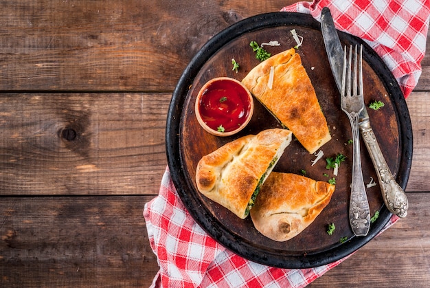 Włoskie jedzenie, zamknięty calzone do pizzy ze szpinakiem i serem, drewniany, widok z góry