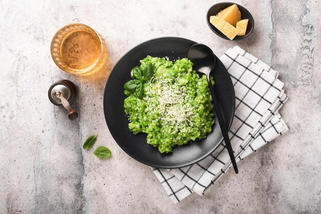 Włoskie risotto Pyszne risotto na białym talerzu z sosem pesto lub pesto z czosnku niedźwiedziego z bazylią, parmezanem i kieliszkiem białego wina na starym jasnoszarym tle stołu Widok z góry z miejscem na kopię