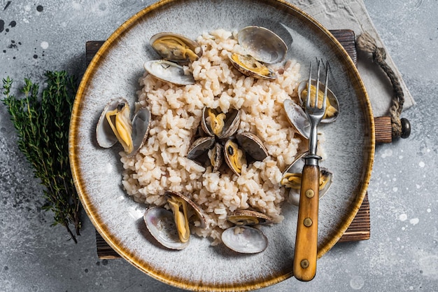 Włoskie risotto z małżami w rustykalnym talerzu z ziołami Szare tło Widok z góry