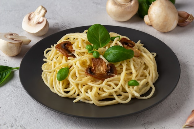 Włoskie spaghetti z pieczarkami i bazylią na ciemnym talerzu na szarej przestrzeni