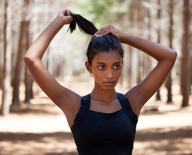 Włosy do góry pozwalają trenować Ujęcie atrakcyjnej młodej kobiety stojącej samotnie na zewnątrz i wiążącej włosy przed treningiem