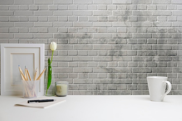Wnętrze biura domowego Ramka na zdjęcia kubek do kawy zeszyt i uchwyt na ołówek na białym stole przy ścianie z cegły Kopiowanie miejsca