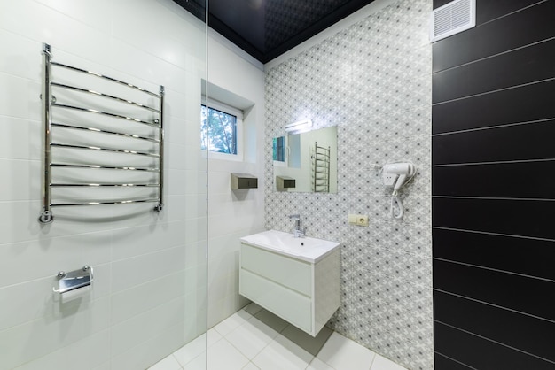 Wnętrze łazienki z umywalką unoszącą się w powietrzu i kabiną prysznicową ze szkła wyłożonego kafelkami w kolorze czarnym