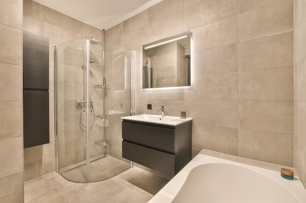Wnętrze łazienki z umywalką wbudowaną w szafkę pod wannę z lustrem oraz kabiną prysznicową otoczoną płytkami