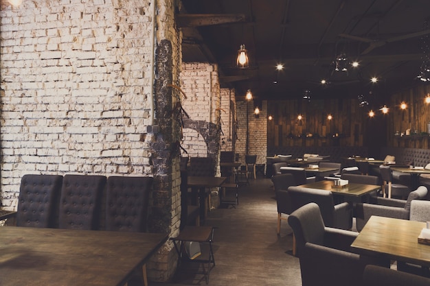 Wnętrze nowoczesnej restauracji. Współczesny design w stylu loft, duży przytulny hol ze stolikami i prywatnymi kabinami z ceglaną ścianą, kopia przestrzeń