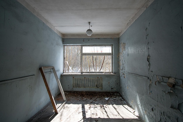 Wnętrze opuszczonego pokoju z rozbitą ramą okna i łuszczącymi się ścianami pomalowanymi na niebiesko w słoneczny dzień