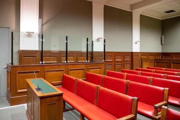 Wnętrze sali sądowej oskarżonego z czerwonymi ławkami dla obrony i widza