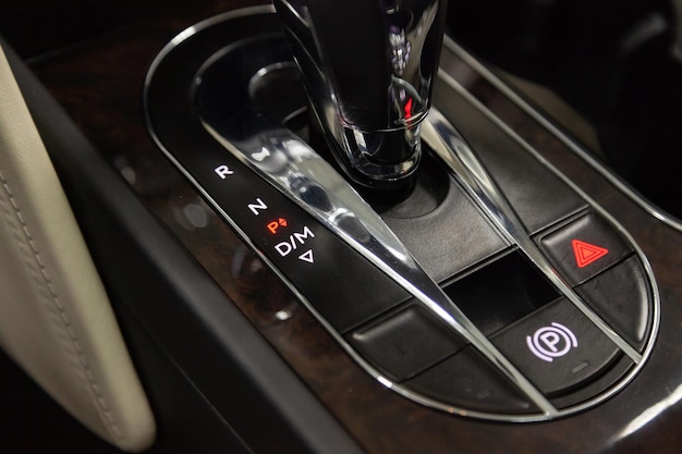 Zdjęcie wnętrze samochodu z widokiem na hamulec postojowy i przyciski awaryjne na desce rozdzielczej i dźwignię zmiany biegów z jasnoszarą skórą