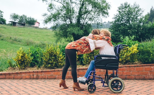 Zdjęcie wnuczka uściska babcię na wózku inwalidzkim w parku
