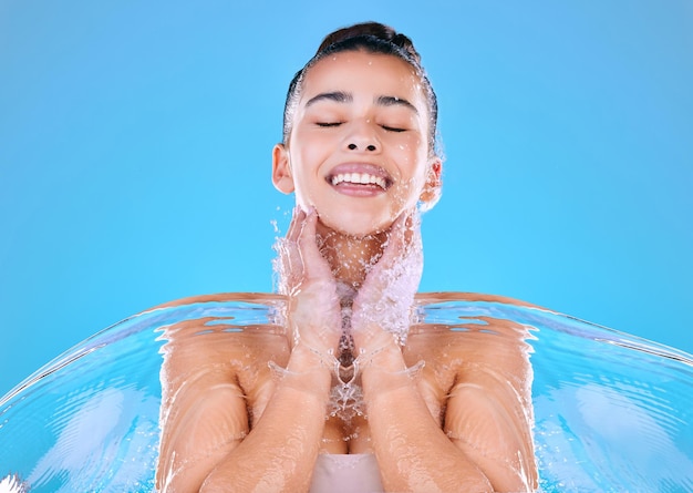 Woda ma właściwości lecznicze. Ujęcie pięknej młodej kobiety opryskanej wodą na niebieskim tle.
