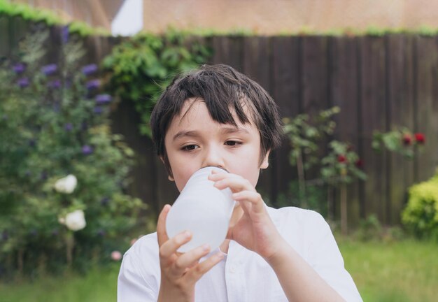 Woda pitna dla dziecka Spragniony chłopiec trzyma butelkę wody Woda pitna dla dziecka podczas zabawy w ogrodzie Światowy Dzień Dziecka Światowy Dzień Środowiska