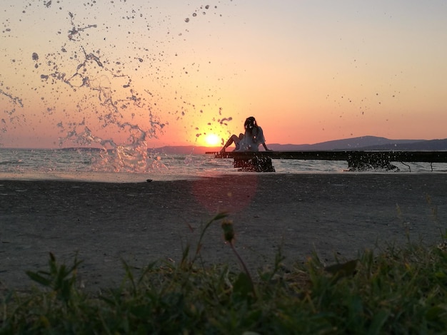 Woda rozpryskana na plaży przez kobietę relaksującą się na molo podczas zachodu słońca