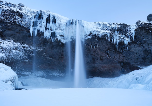 Wodospad Seljalandsfoss Islandia Islandzki zimowy krajobraz Wysoki wodospad i skały Śnieg i lód Potężny strumień wody z klifu Popularne miejsce do podróżowania na Islandii