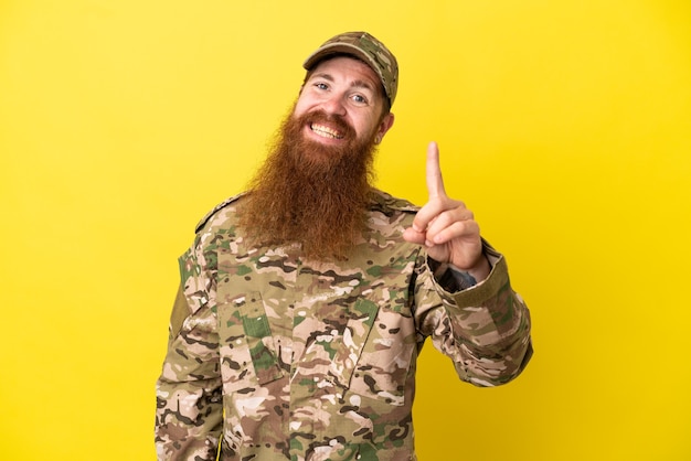 Wojskowy rudy mężczyzna na białym tle na żółtym tle pokazując i podnosząc palec na znak najlepszych