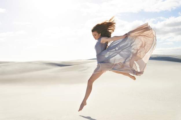 Wolność i izolacja na plaży Widok z boku na piękną młodą kobietę w powiewającej sukience skaczącej po piasku
