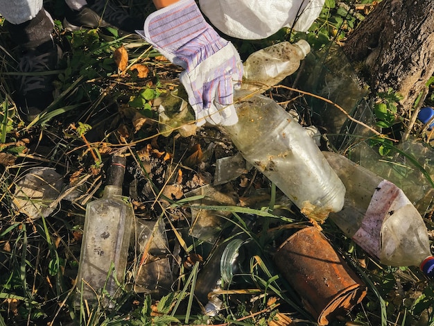 Wolontariusz zbiera brudne plastikowe butelki w parku Ręka kobiety w rękawiczce zbiera śmieci zbieranie śmieci w torbie Sprzątanie przyrody z plastiku jednorazowego użytku