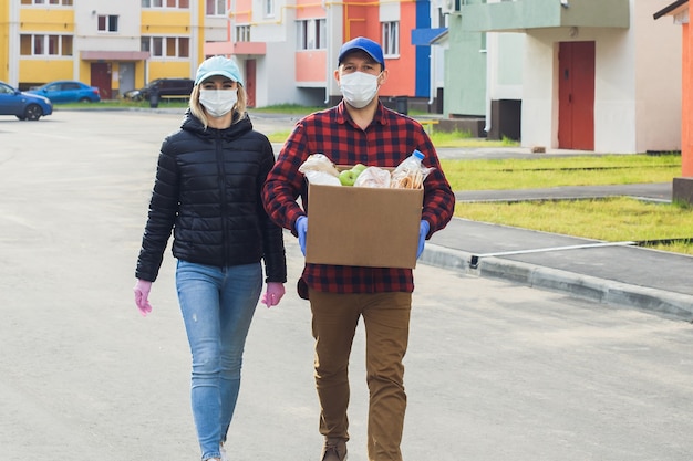 Wolontariusze w ochronnych maskach idą ulicą z pudełkiem zakupów, dobroczynności.