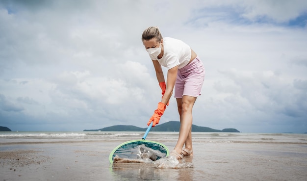 Wolontariuszka-ekolożka czyści plażę nad brzegiem morza z plastiku i innych odpadów