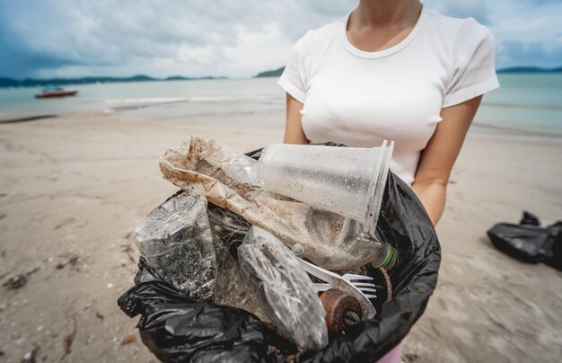 Wolontariuszka-ekolożka czyści plażę nad brzegiem morza z plastiku i innych odpadów